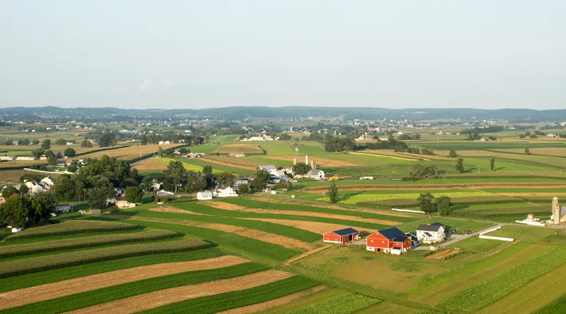 Aerial view of Lancaster County, Pennsylvania farmland with red barns, silos, white farmhouses and a small town in the distance