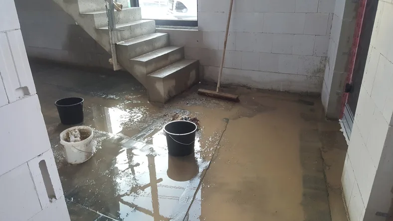 Flooded basement with standing muddy water pooled across the concrete floor and stairs