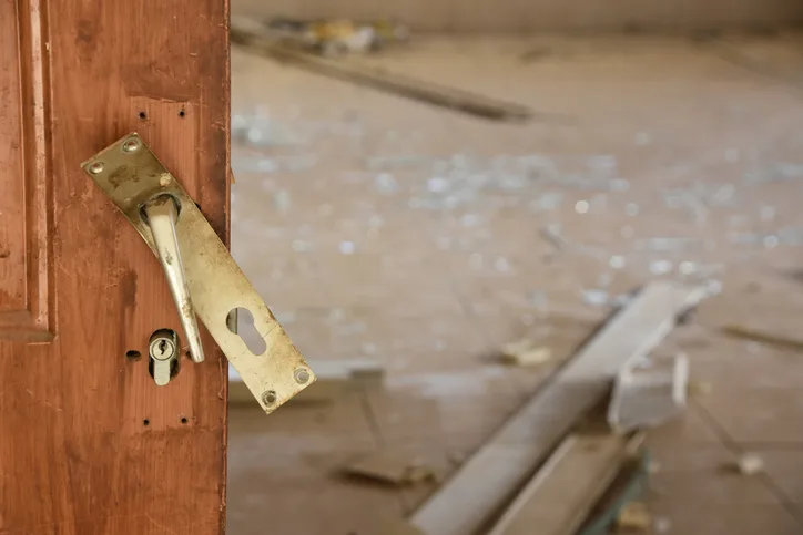Open interior door with damaged brass lock hardware revealing a ransacked room littered with debris