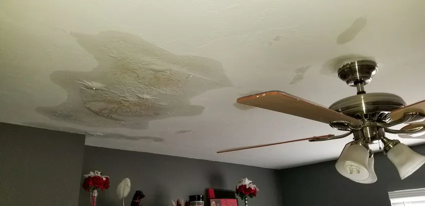 Brown water stains spreading across a bedroom ceiling from a roof leak above
