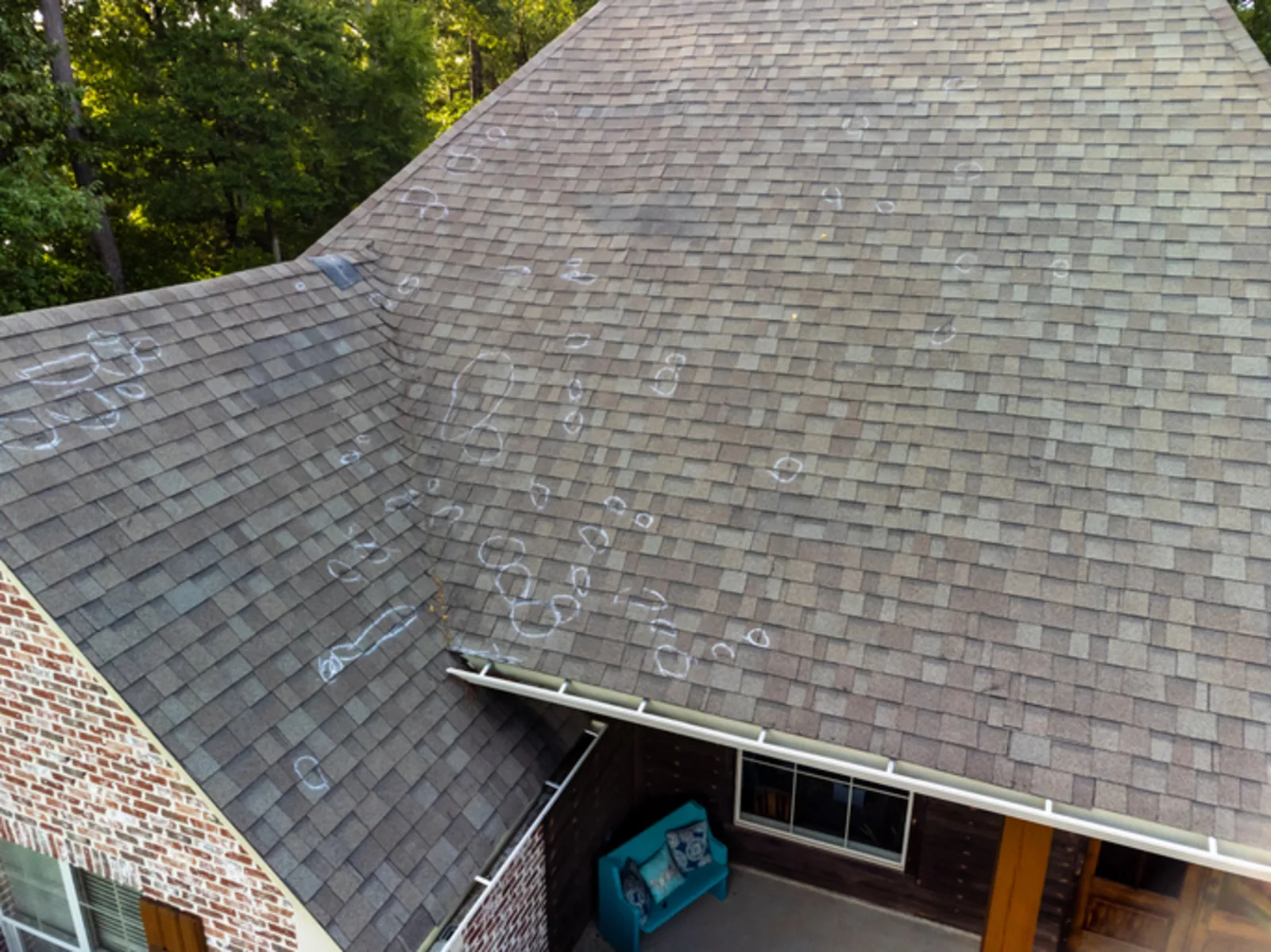 Asphalt shingle roof with individual hail impact marks circled in white chalk during a hail damage claim inspection