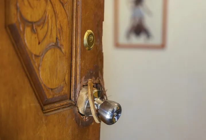 Splintered wooden entry door and damaged deadbolt hardware after a forced-entry burglary