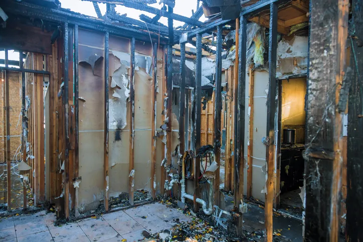 Gutted interior with burned wall studs and peeling drywall inside a fire-damaged house